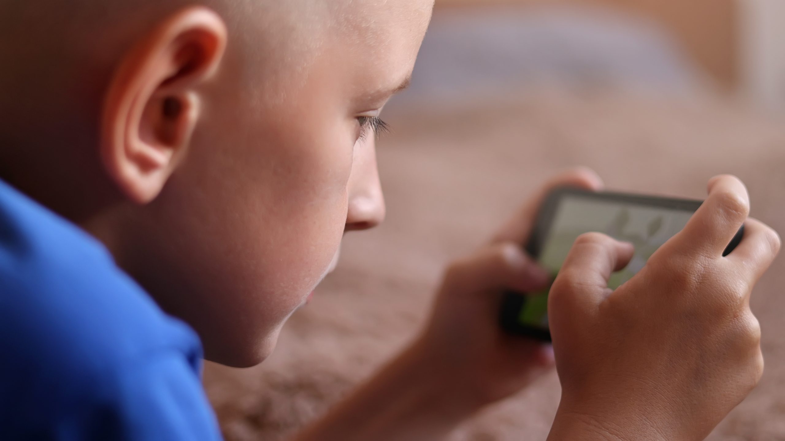 Preschool boy at Home is Lying on the bed, using a Smartphone. Child playing video games on a cellphone, Browses Internet, Views Content, Videos. Shooting wit camera over your shoulder