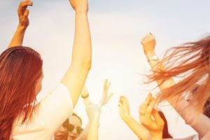 Group of young happy dancing tan girls on blue sky background, summer time, open air party